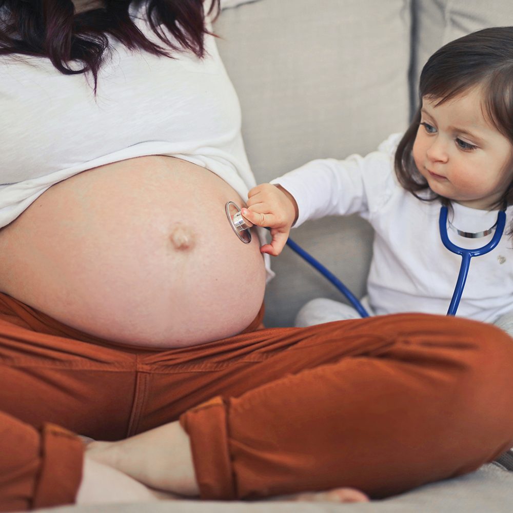 little girl listens with a stethoscope in the belly of pregnant mom